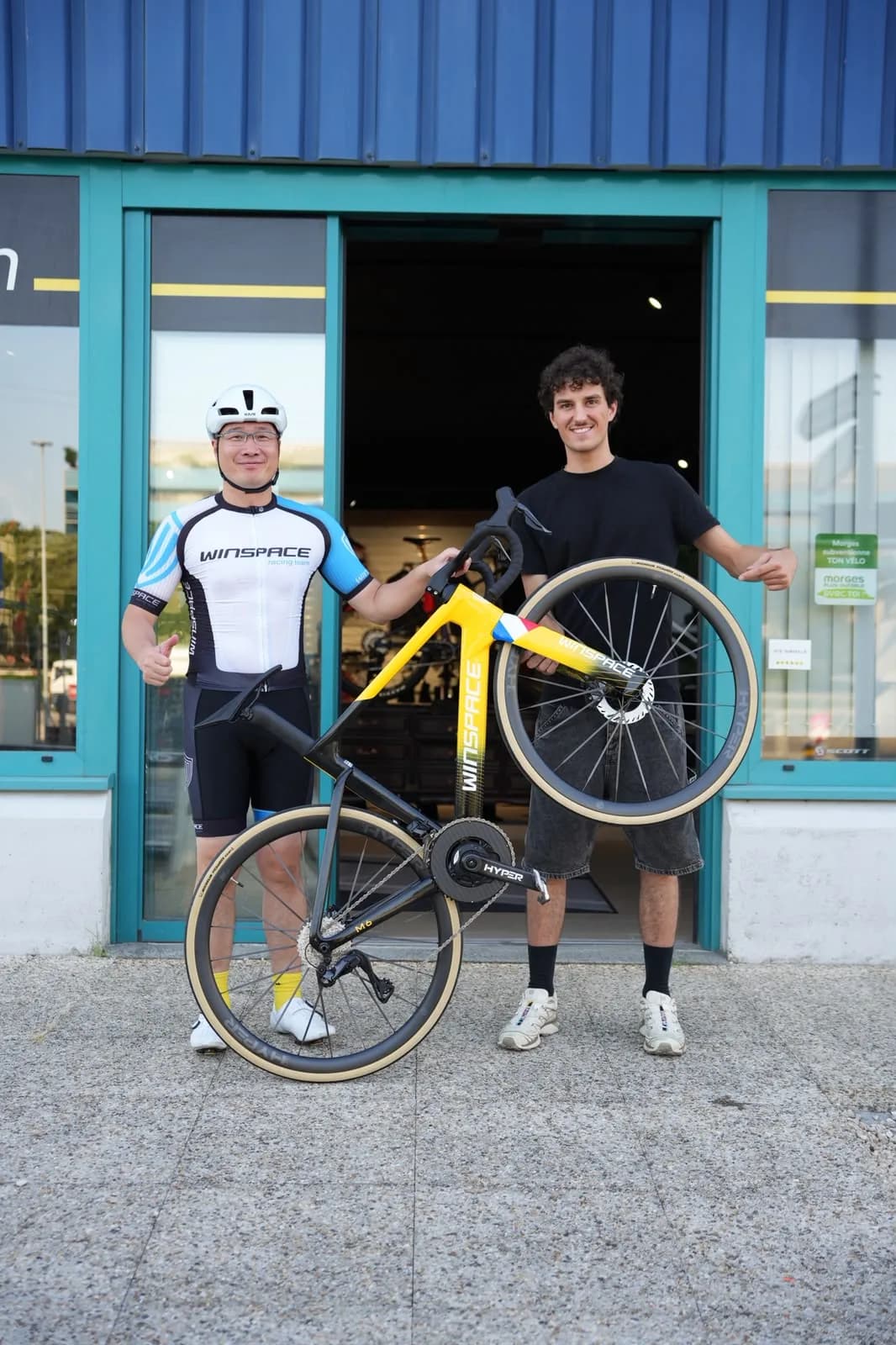 Stephen, CEO de Winspace, avec le mécanicien Gilles et le vélo Winspace M6 aux couleurs du Tour de France devant l'atelier Cycles Dotti à Morges